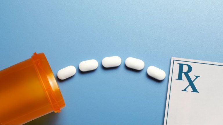 White pills spilling out of a medicine bottle, on a blue surface.