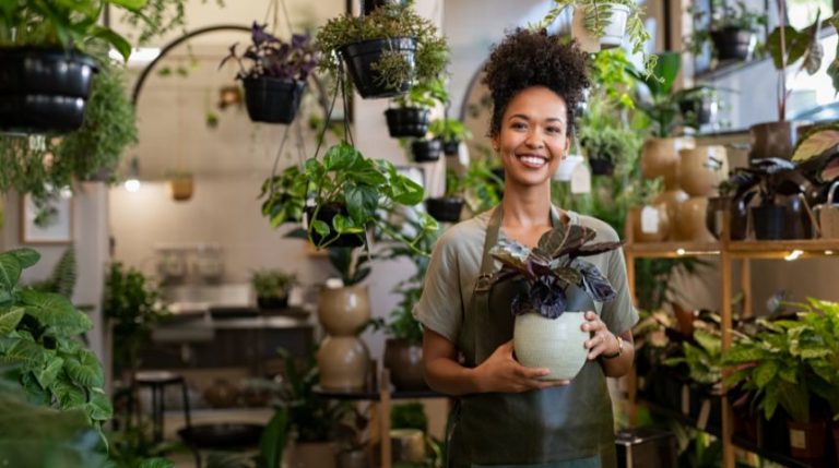 A small business owner holding a potted plant in their store.