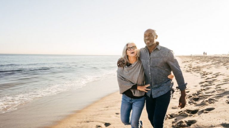 A retired couple walking on a beach together.