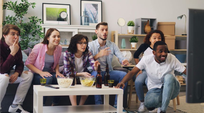 A group of friends sitting together in a living room, watching a live sports game on TV.