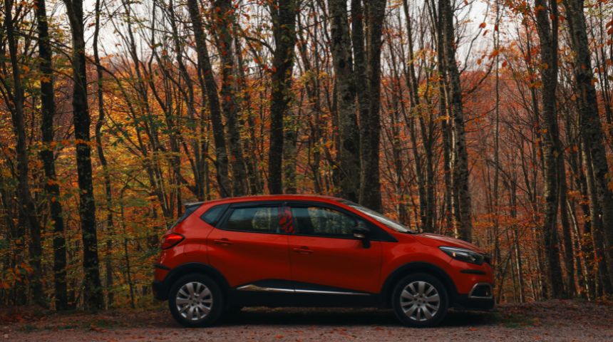 A red hybrid SUV parked in front of trees.