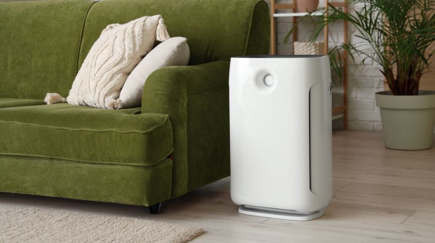 A white air purifier beside a green couch.