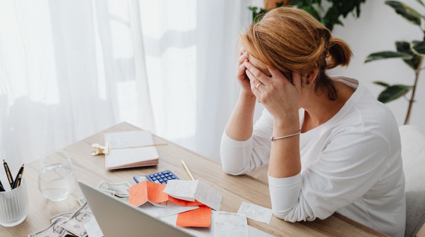 A woman sitting at a desk, holding her head in her hands. She looks stressed.